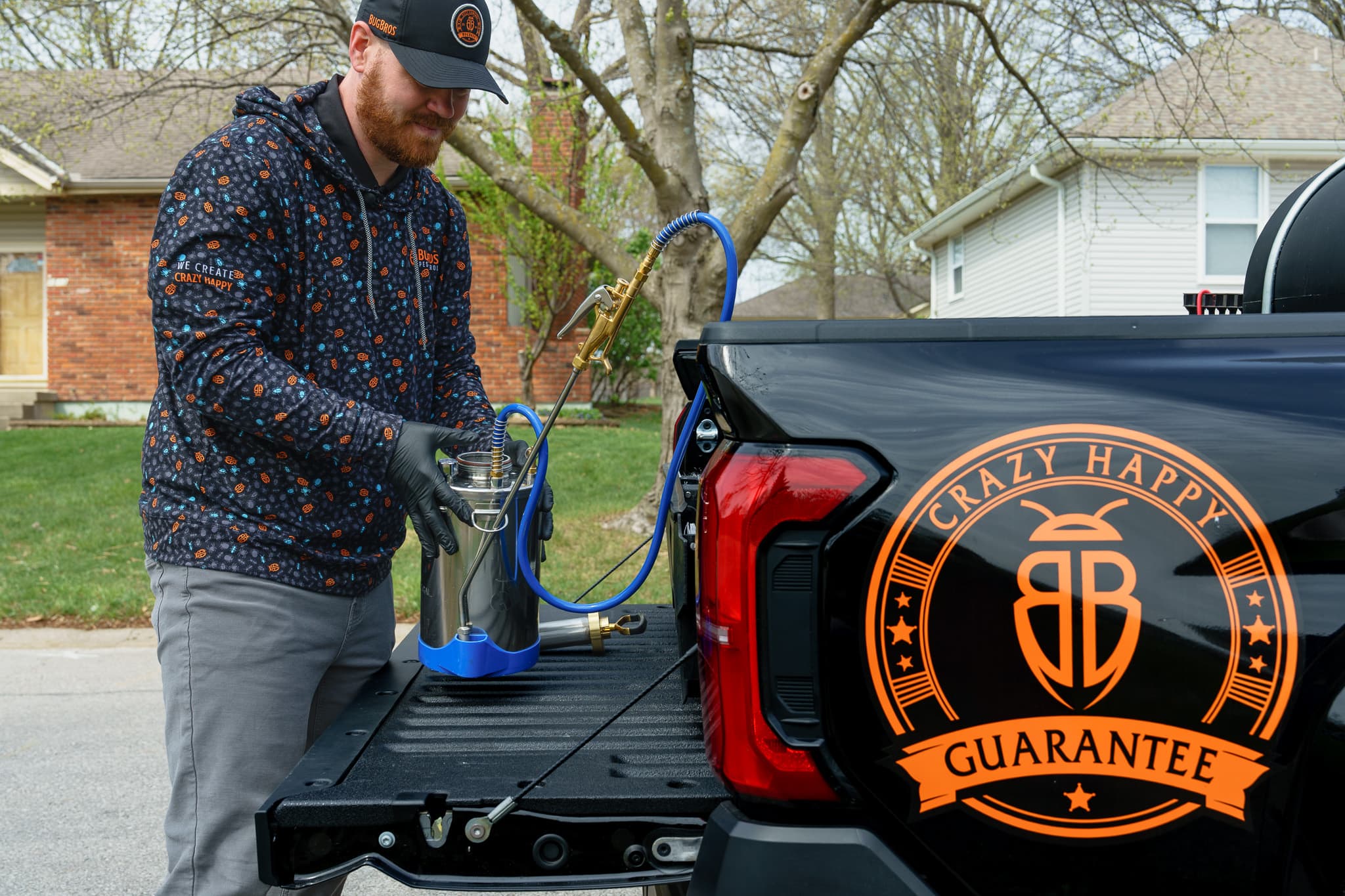 BugBros Pest Control technician loading professional spray equipment at the tailgate of a branded truck in a Kansas City neighborhood
