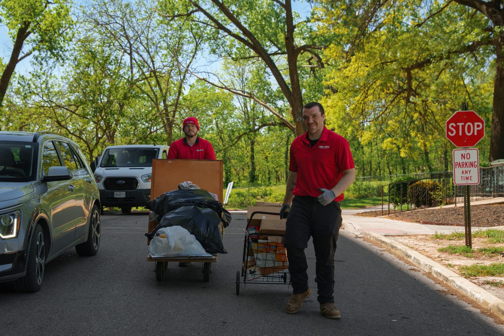 Junk King crew hauling a load on a residential street, both in uniform and smiling at the camera